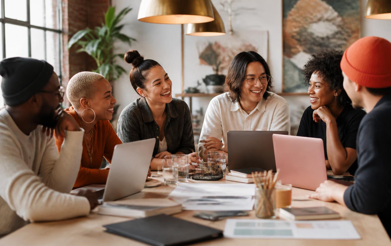 A racially diverse group of creative entrepreneurs laughing together around laptops