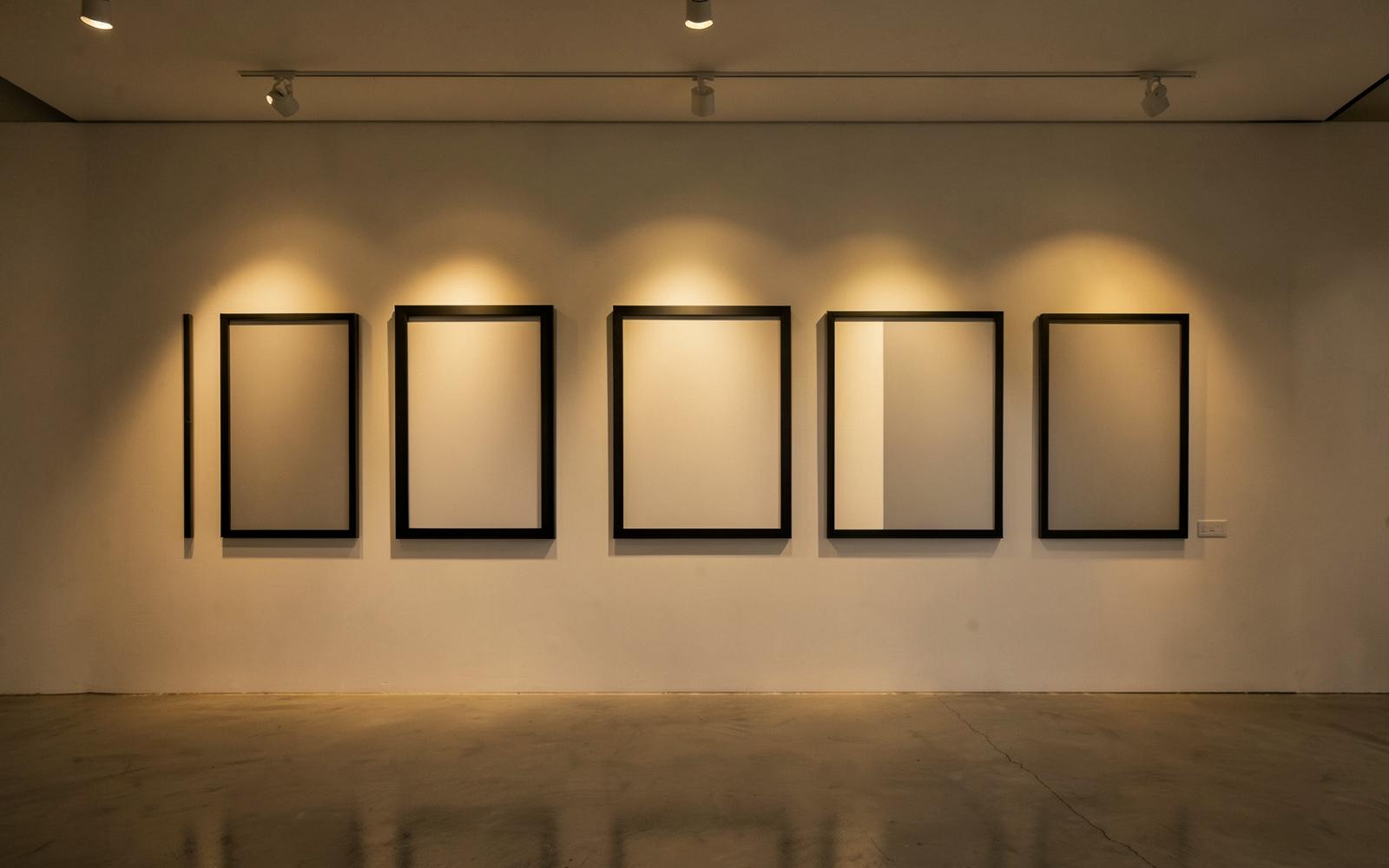 An empty gallery wall of blank black frames lit by warm spotlights, waiting to be filled